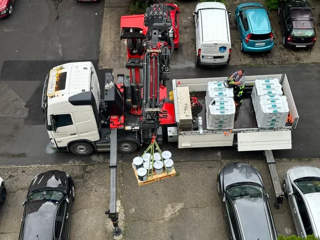 Darus teherautó csomagolt anyagot emel a parkolóban álló autók között