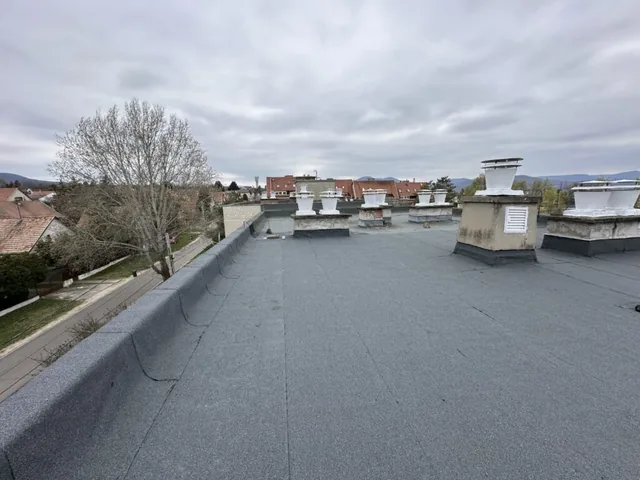 Sötétszürke bitumenes lapostető fehér szellőzőkéményekkel és peremfallal
