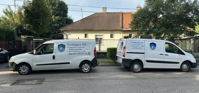 Két fehér Tetőpajzs-kisteherautó fák alatt egy lakóutcában